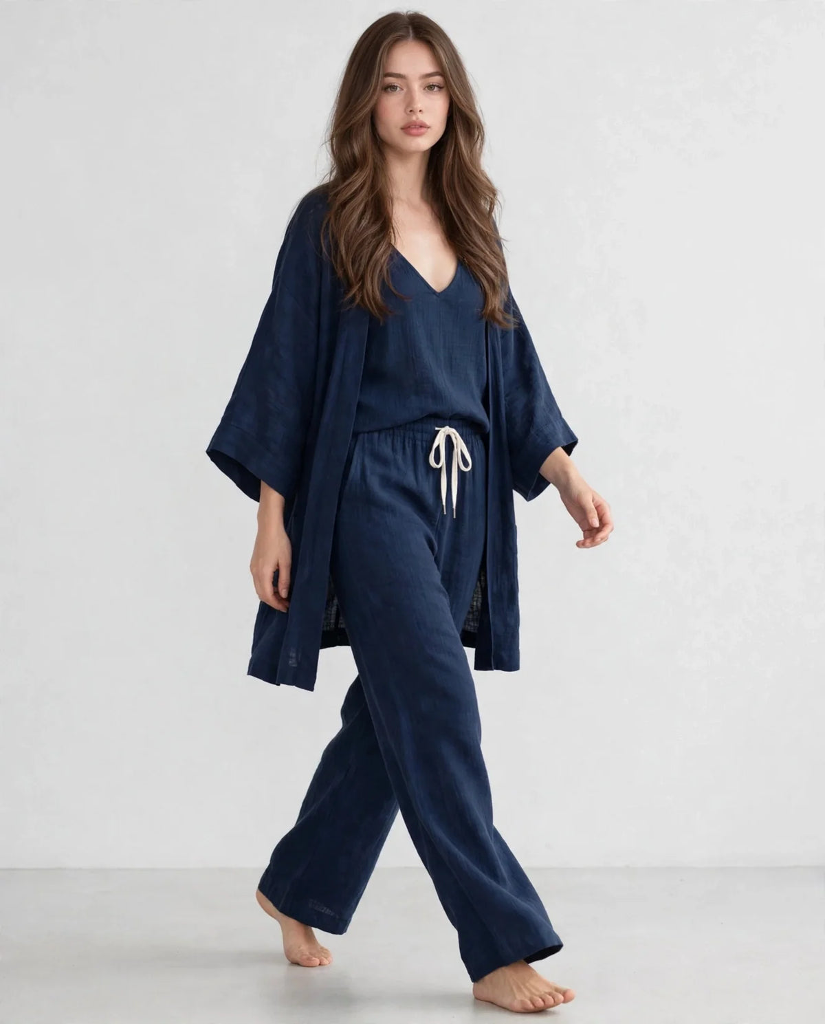 Woman in a navy V-neck top, open cardigan and drawstring pants set, walking pose, light gray studio background.