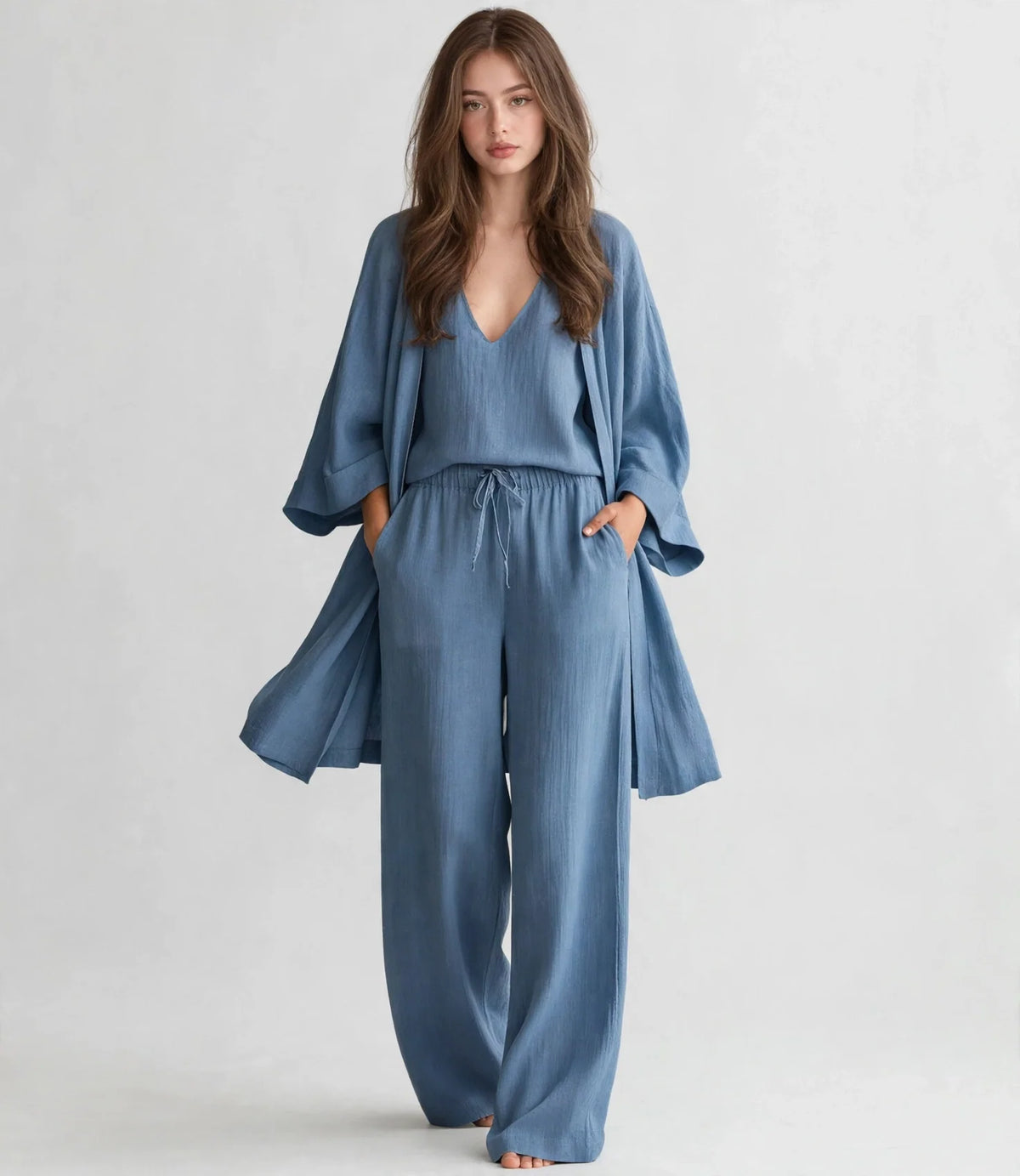 Woman in a dusty blue V-neck top, open cardigan and drawstring pants set, walking full-length pose, gray studio background.