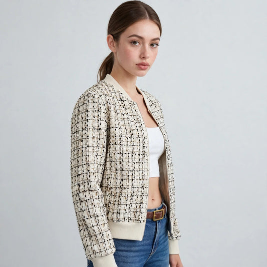 Three-quarter view of a woman wearing an open tweed bomber jacket, white crop top, jeans, and a brown belt.