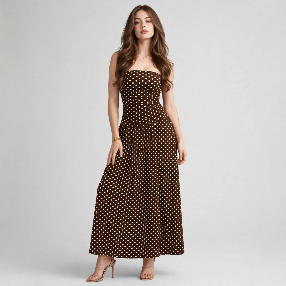 Front view of a brown polka dot strapless maxi dress with smocked bodice and flowy skirt, white studio backdrop.
