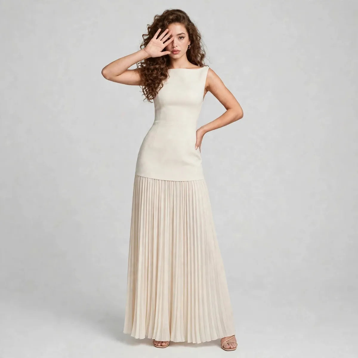 Full-length front view of a cream sleeveless maxi dress with fitted bodice and flowing pleated skirt in a gray studio.