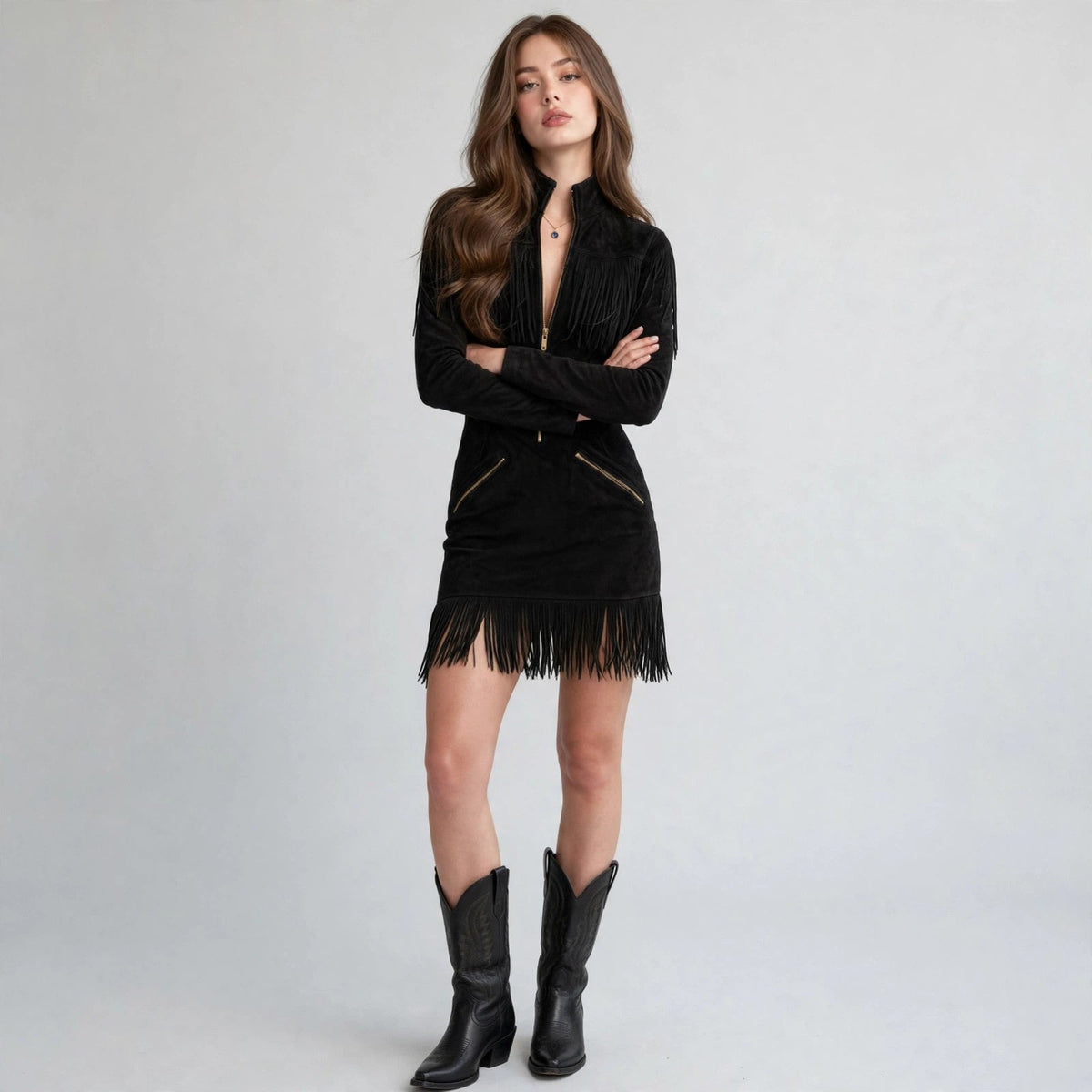 Woman modeling a black fringe mini dress with gold front zipper, high collar and long sleeves, with black cowboy boots.