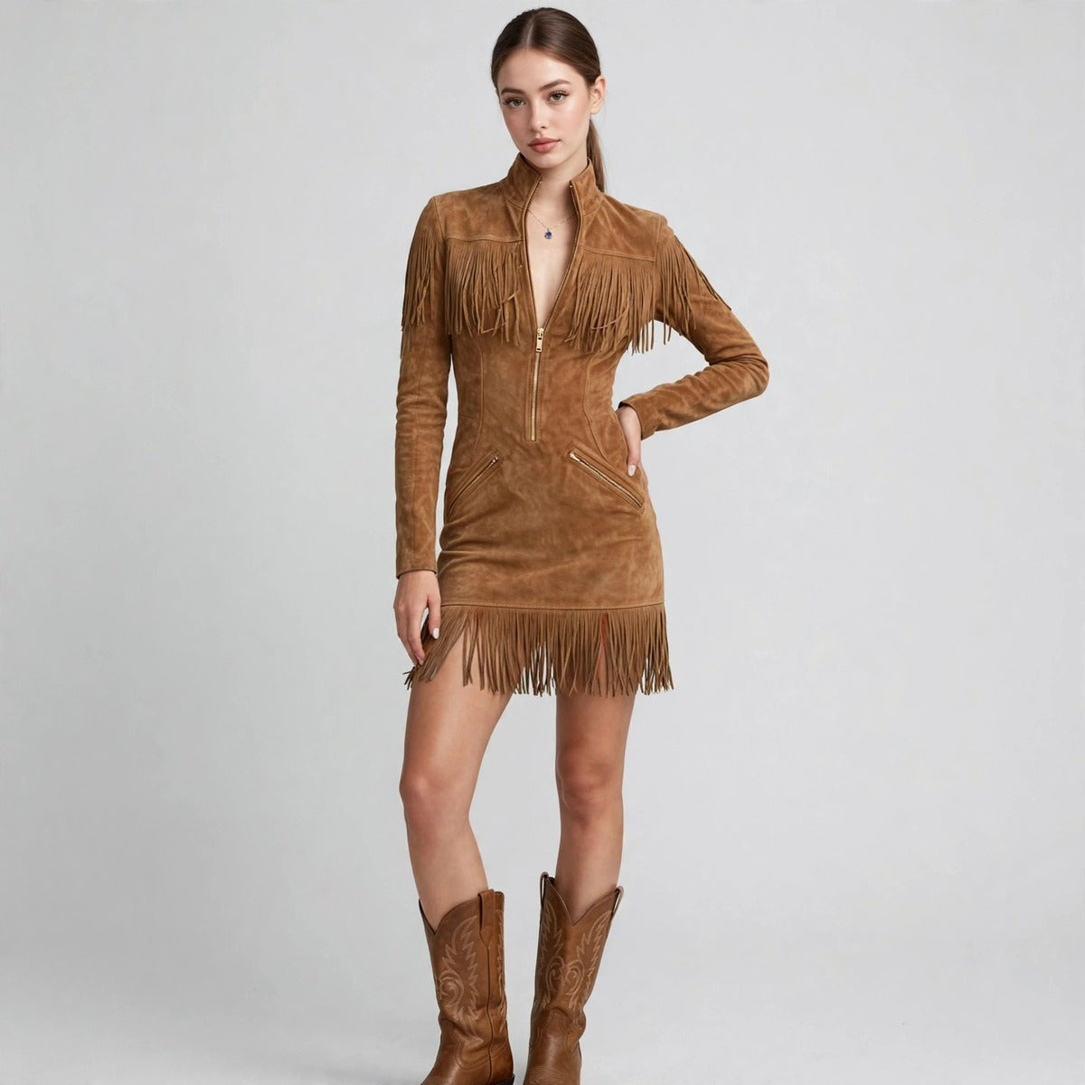 Woman modeling a tan suede mini dress with fringe trim, front zipper and long sleeves, paired with brown cowboy boots.