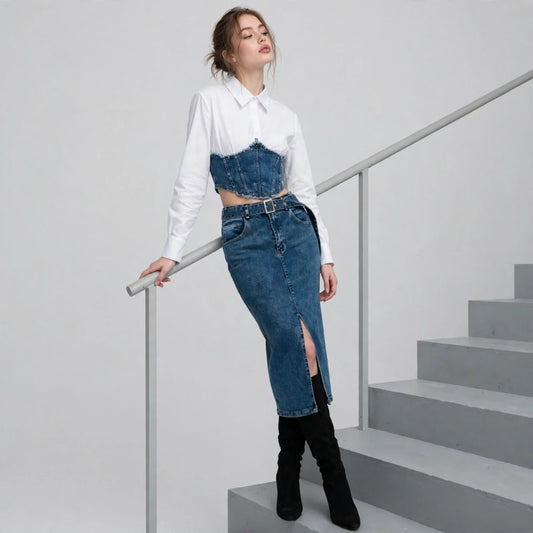 Woman leaning on stair railing in white shirt, denim corset top, dark denim slit midi skirt, black boots, light backdrop.