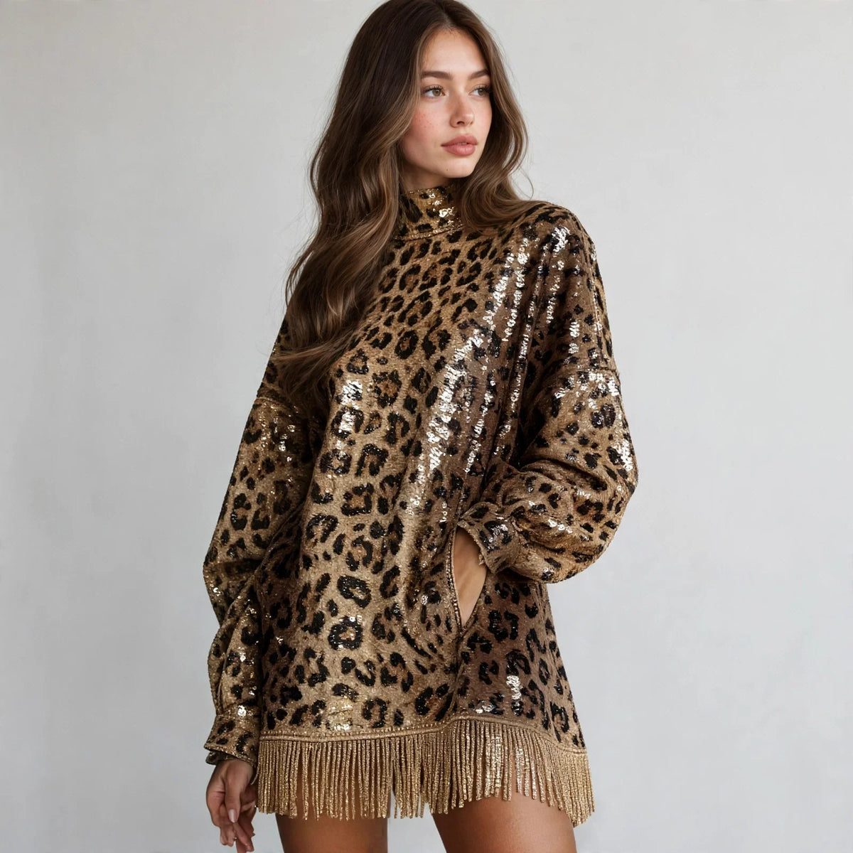 Model in a gold leopard sequin mock neck mini dress with long sleeves and fringe hem, standing pose, white studio background.