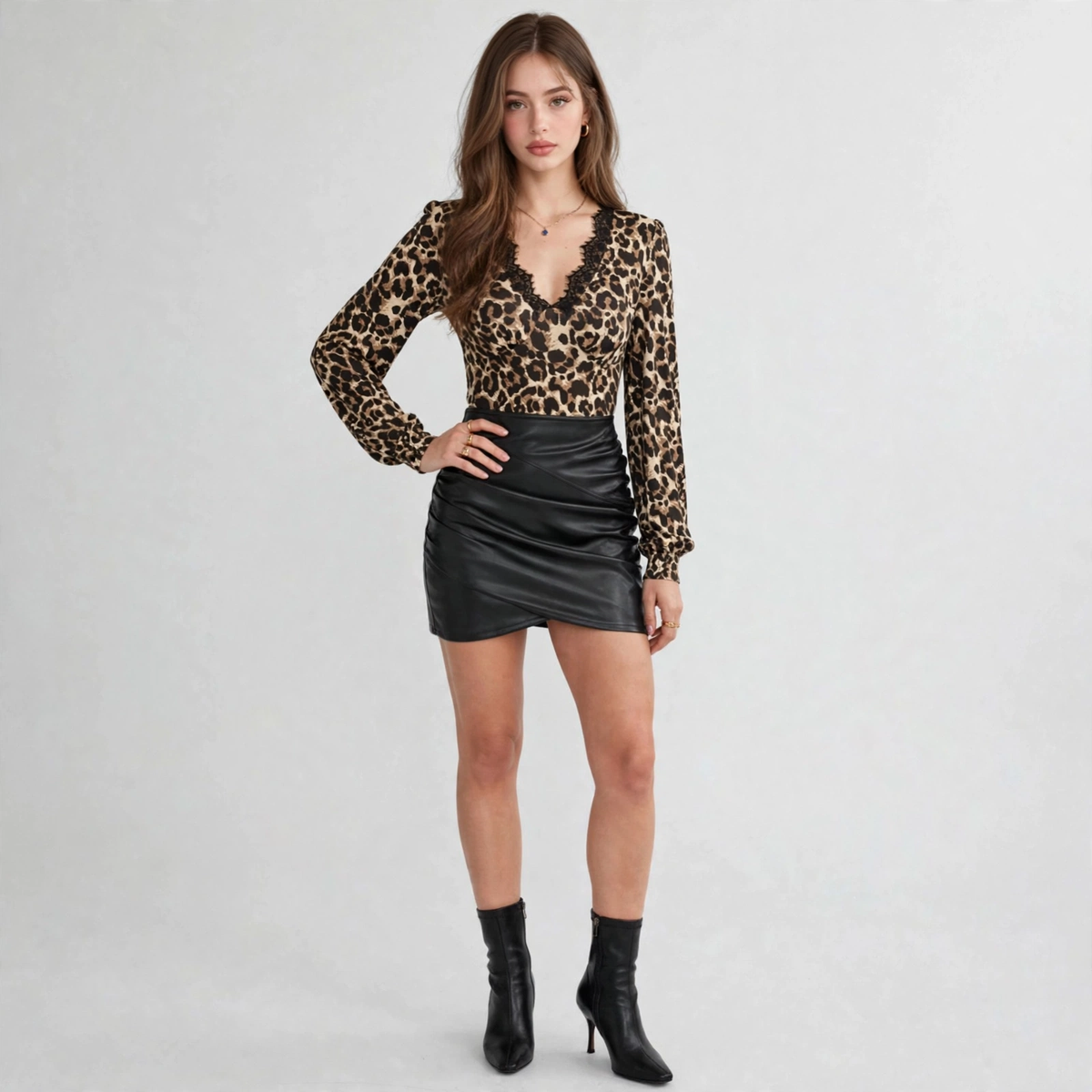 Woman in a leopard print long-sleeve top with black lace V-neck trim, black faux-leather skirt and boots, gray background.