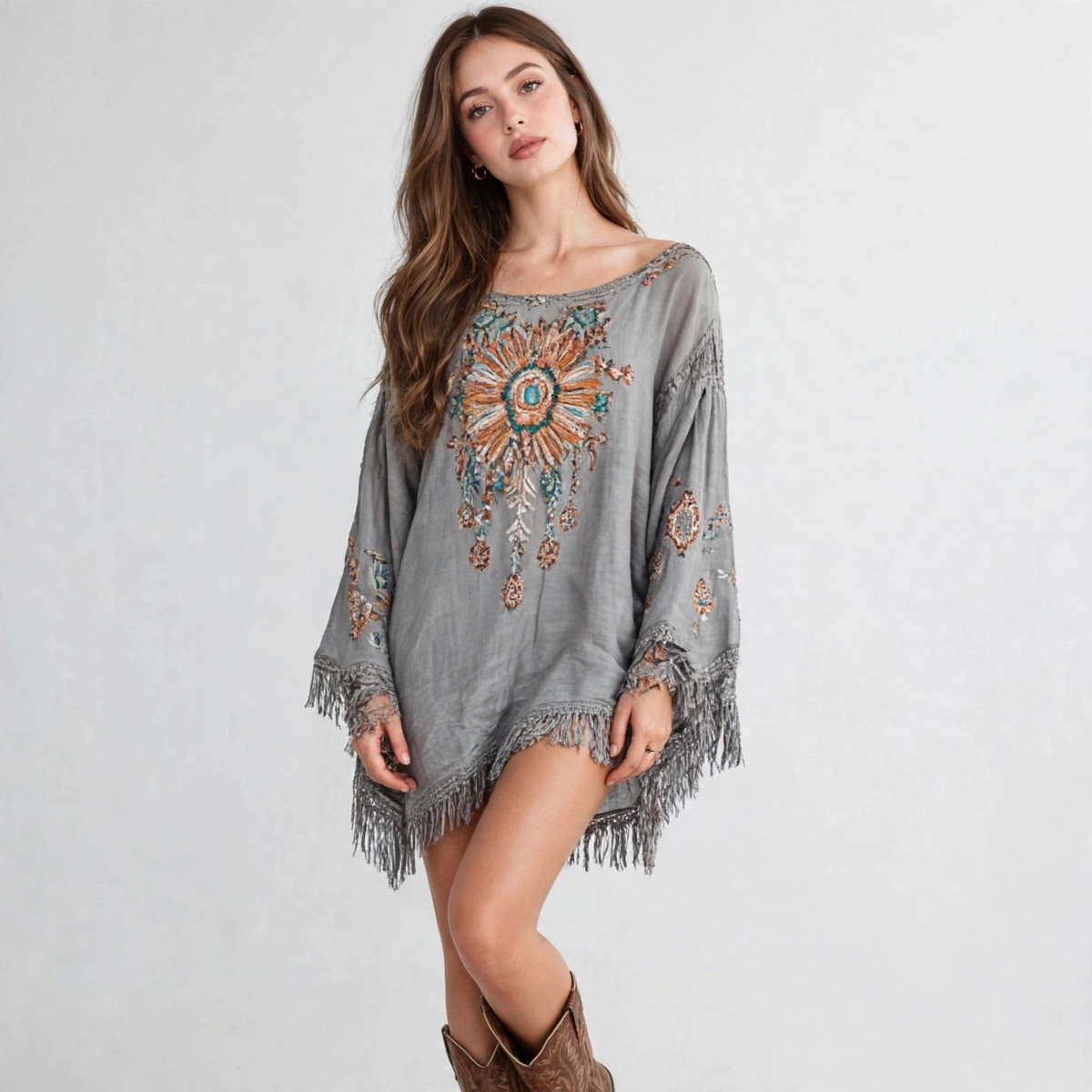 Model standing in a grey embroidered long-sleeve mini dress with fringe hem and bell sleeves, brown boots, white background.