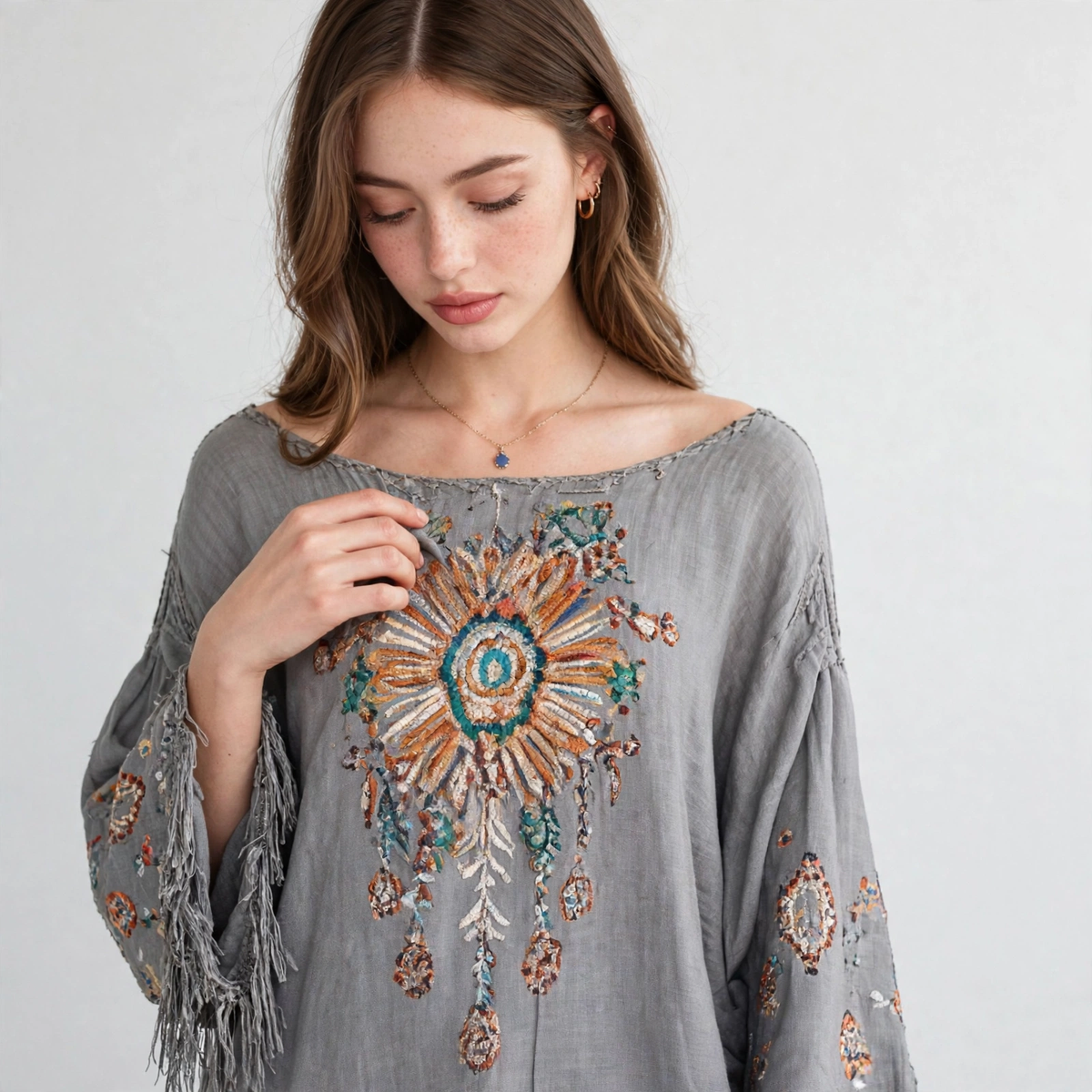 Close-up of a grey long-sleeve mini dress with colorful floral chest embroidery, wide scoop neckline and fringed bell cuffs.