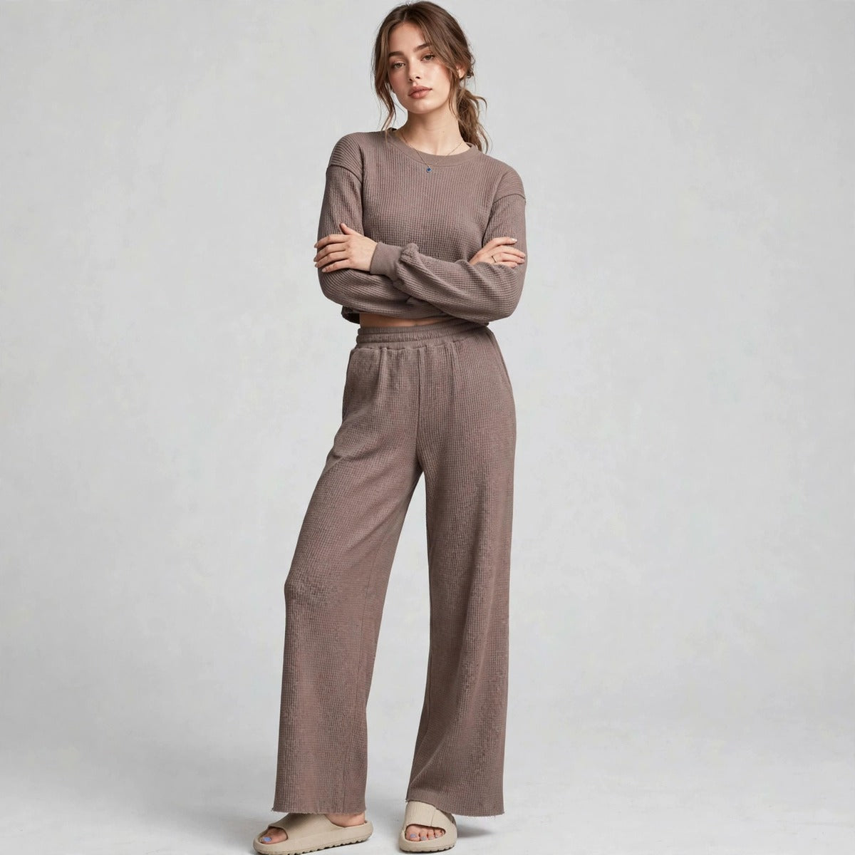 Model with arms crossed in brown waffle-knit cropped top and wide-leg pants set, front view, light grey studio backdrop.