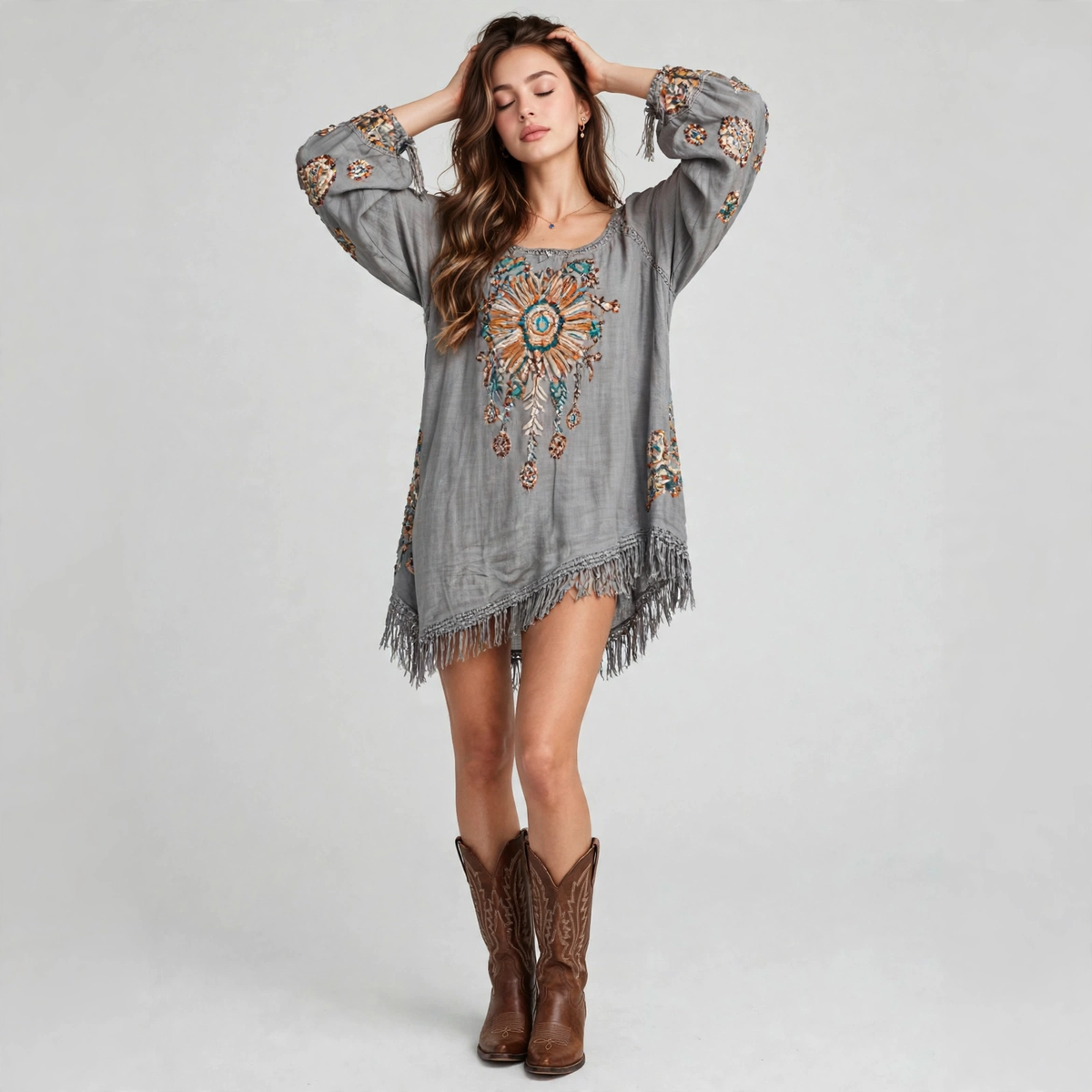 Full-length view of a grey embroidered fringe-hem mini dress with wide neckline, bell sleeves, hands in hair, white backdrop.