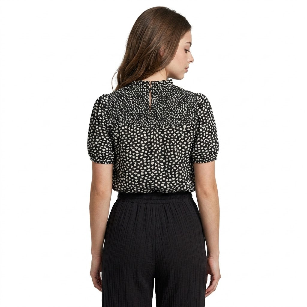 Back view of black printed puff sleeve blouse with white dot pattern, mock neck keyhole button detail, worn with black pants.