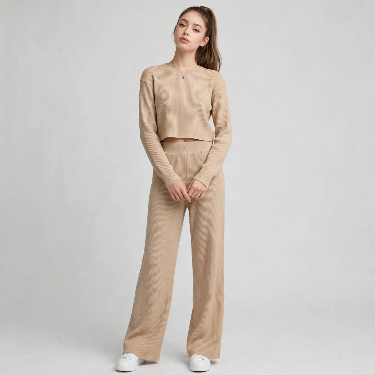 Model in beige waffle-knit cropped top and wide-leg pants set with hands clasped, front view, light grey studio backdrop.