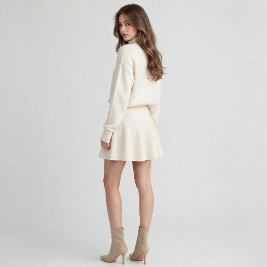 Back three-quarter view of a cream turtleneck sweater and flared mini skirt set with beige ankle boots, gray studio.