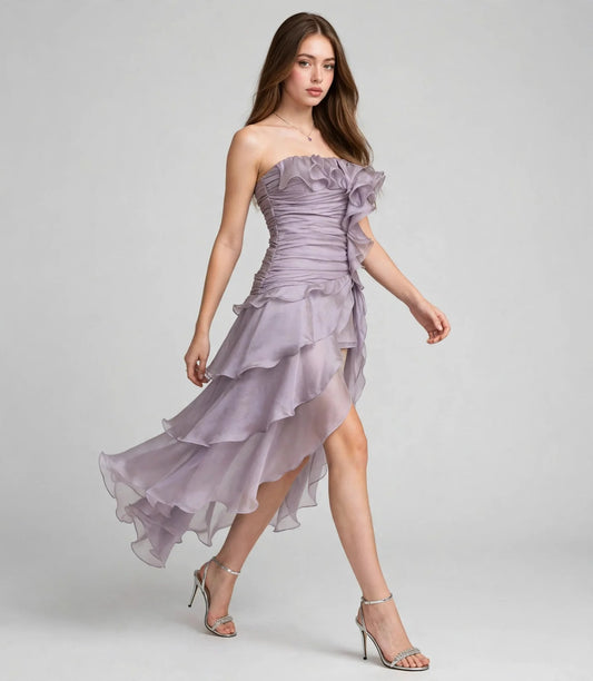 Woman walking in a lavender chiffon strapless dress with ruffled tiered skirt and silver heels, gray studio background.
