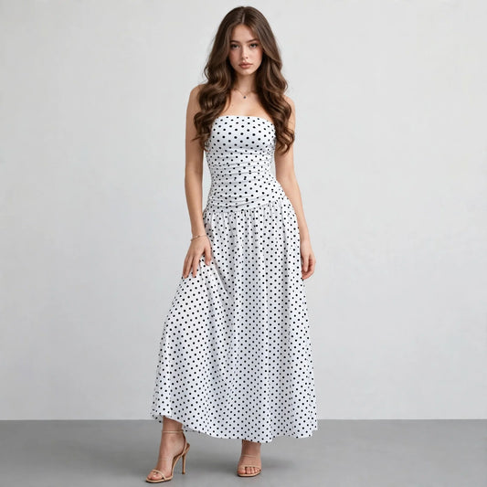 Front view of a white polka dot strapless maxi dress with smocked bodice and flowy skirt, white studio backdrop.