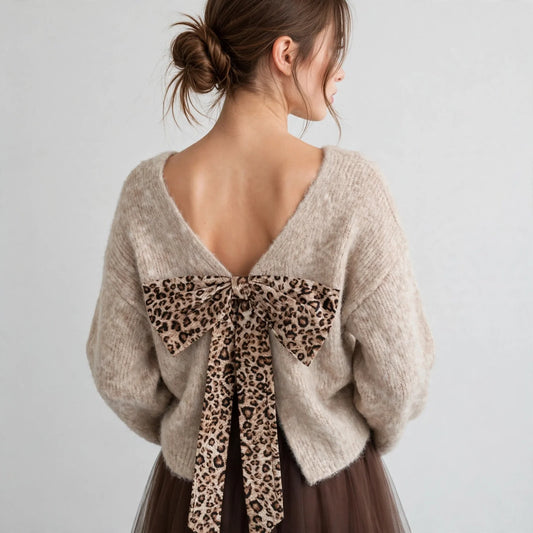 Back view of beige fuzzy dropped-shoulder sweater with leopard-print bow tied at open back neckline, close-up, studio shot.