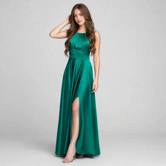 Woman in an emerald green satin halter gown with high slit and fitted waist, hand on head, gray studio background.