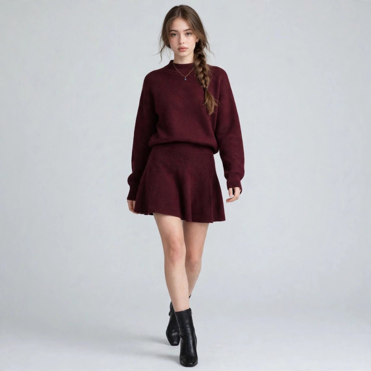 Woman walking in a burgundy knit sweater and matching flared mini skirt set with black ankle boots, gray studio.