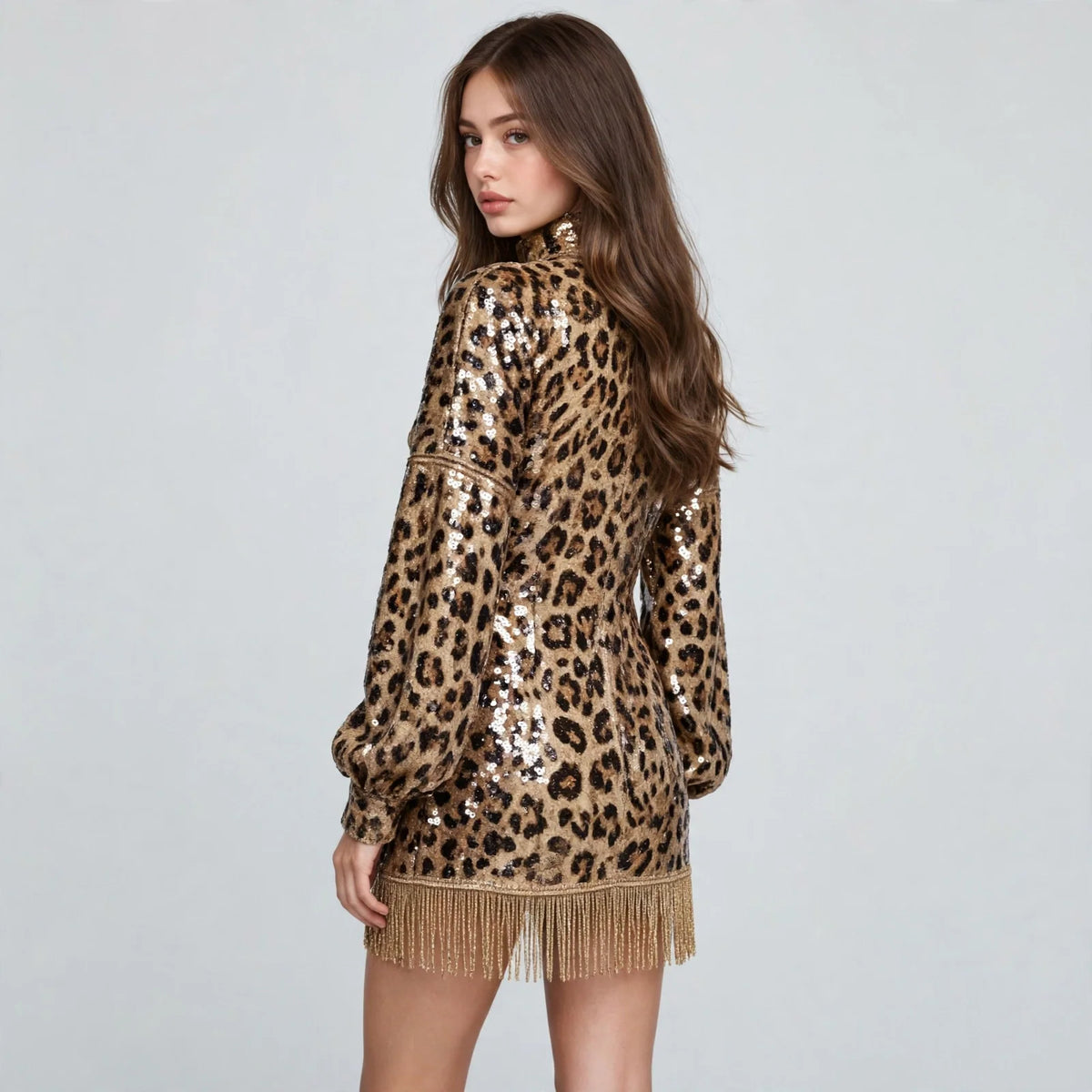 Back three-quarter view of a leopard sequin mock neck mini dress with balloon sleeves and fringe hem, white studio backdrop.