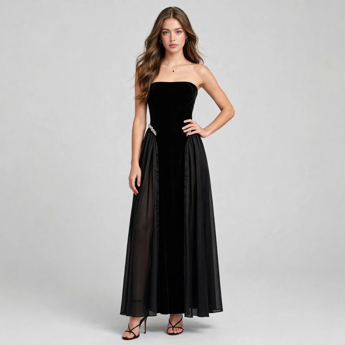 Front view of model with hand on hip wearing black strapless maxi dress with flowing skirt, grey studio background