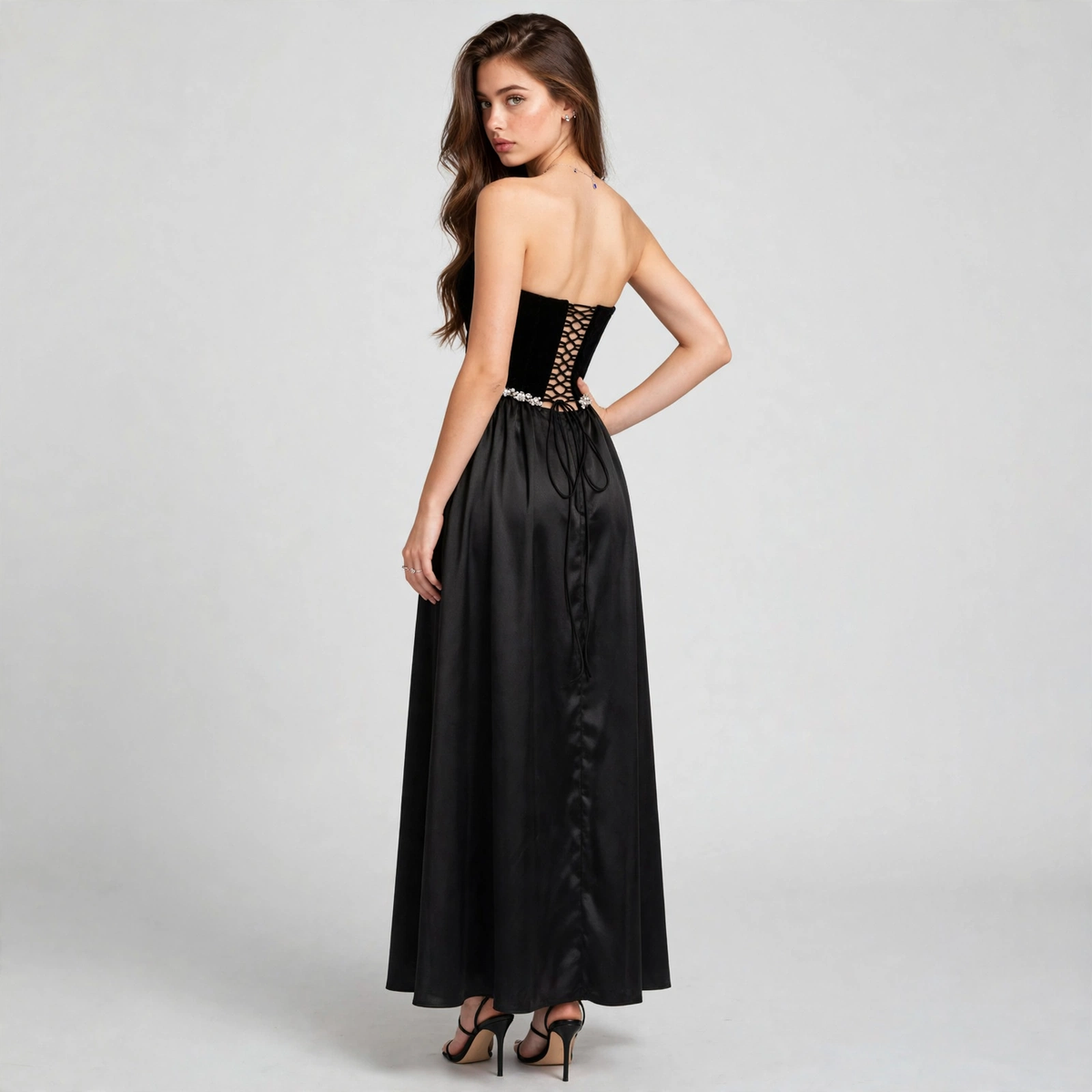 Back view of a woman in a black strapless maxi dress with a lace-up corset back, beaded waistband, flowing skirt.