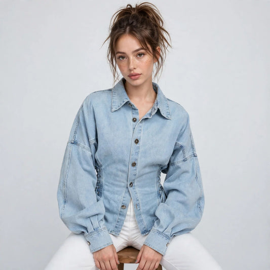 Woman seated wearing a light-wash denim jacket with button front and lace-up sides, white pants, white studio background.