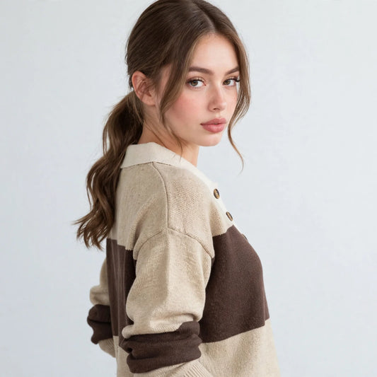 Three-quarter view of woman with ponytail in beige and brown color-block polo sweater, blue jeans, light studio backdrop.