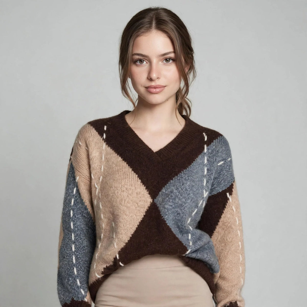 Upper-body view of a woman in a brown argyle V-neck oversized sweater with beige and gray diamonds, gray background.