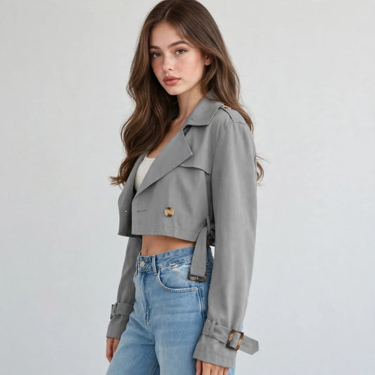 Model in a gray cropped double-breasted jacket over a white crop top and jeans against a light gray studio background.