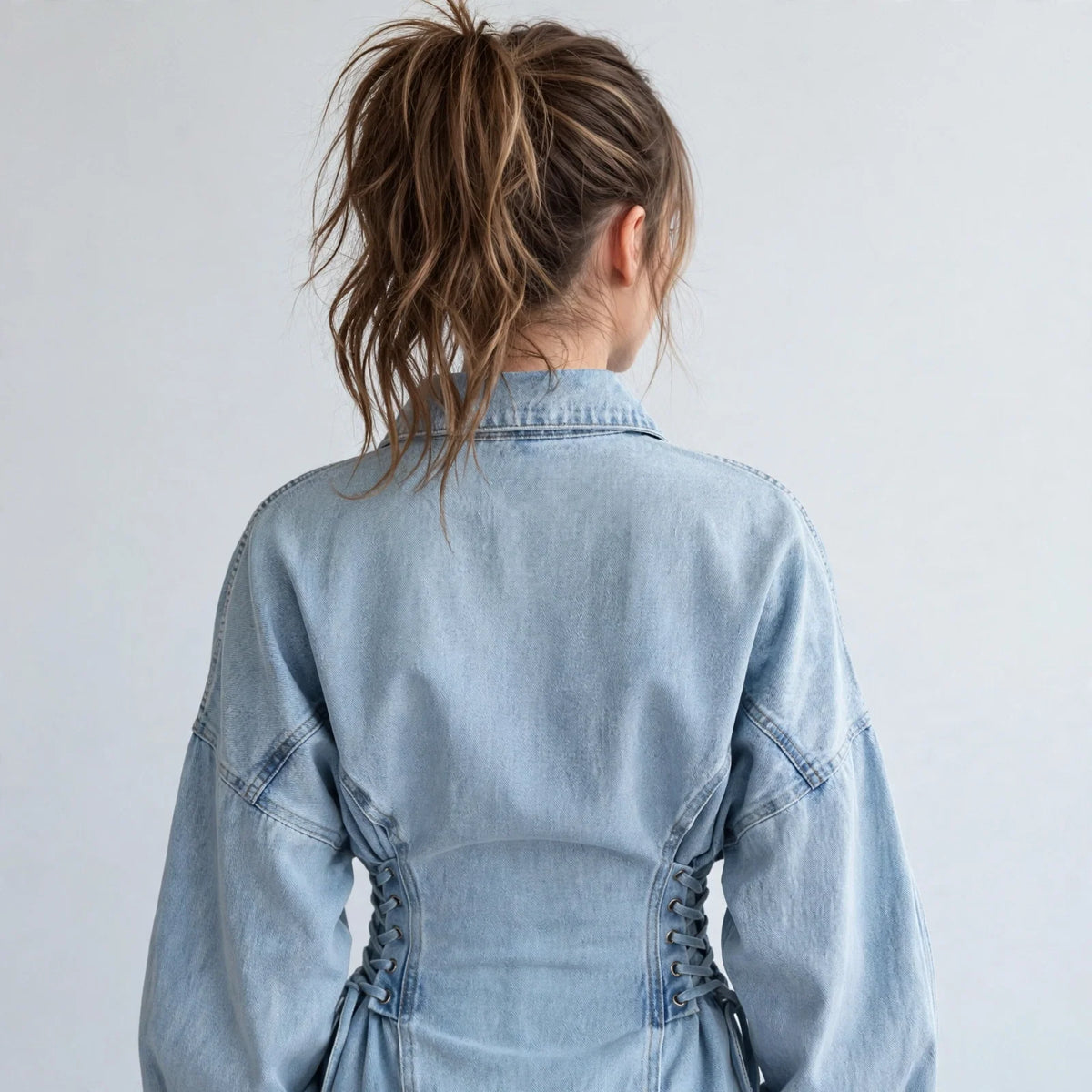 Back view of a light-wash denim jacket with lace-up side details and balloon sleeves, white studio background.