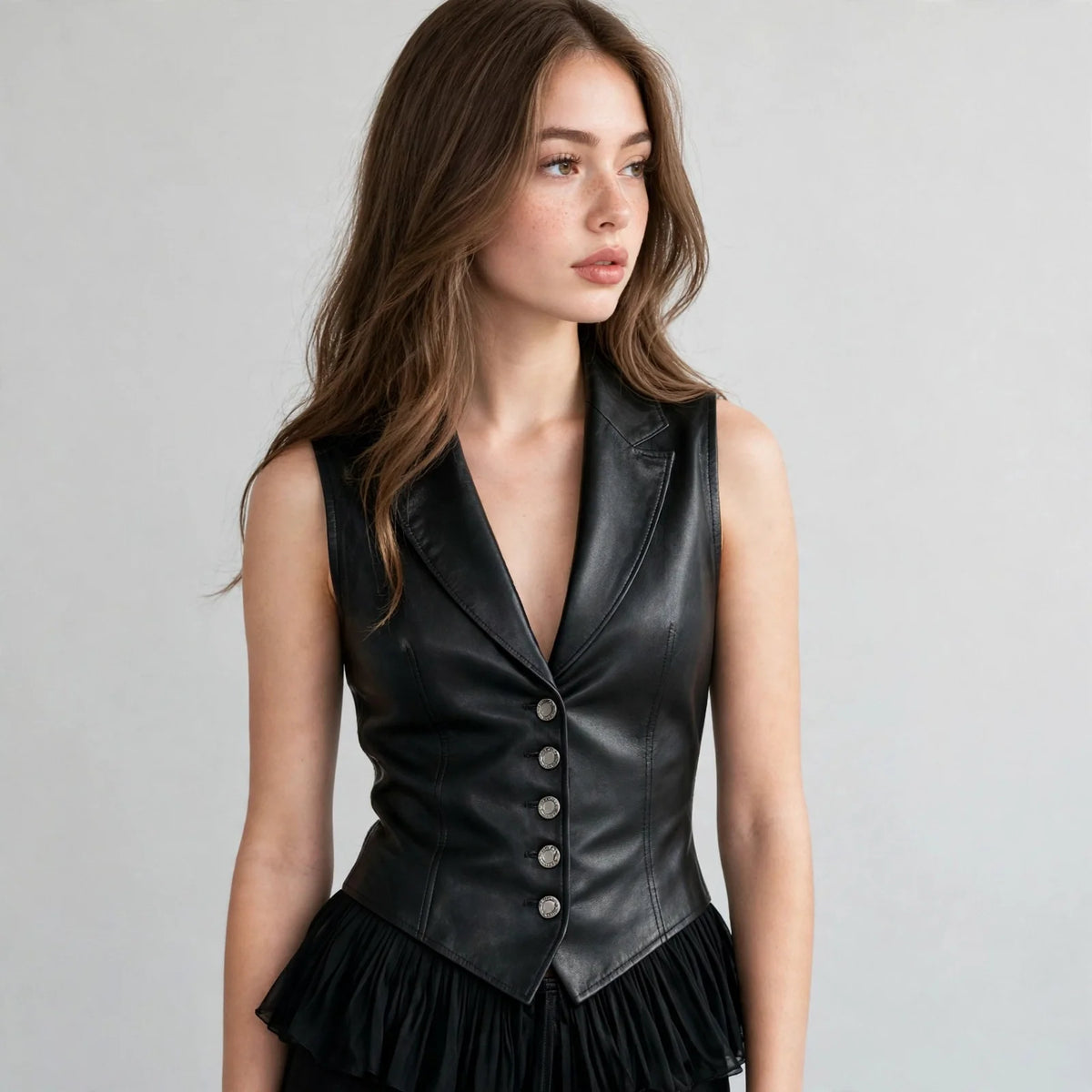 Close-up front view of a black sleeveless faux leather vest coat with lapel collar and button front, gray studio background.