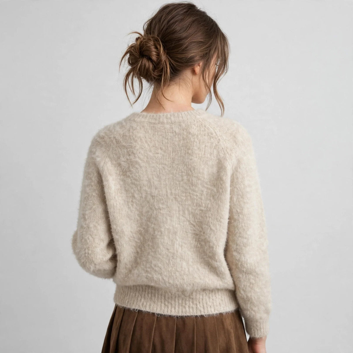 Back view of a beige argyle raglan sleeve knit sweater, model with hair up, brown skirt, white studio background.