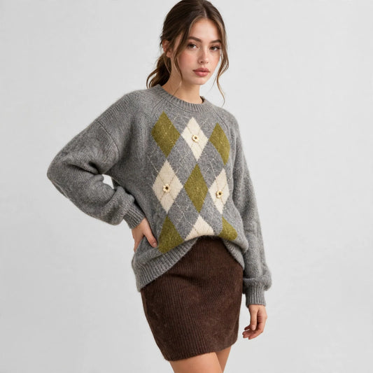 Model in a grey argyle raglan sleeve sweater with olive and cream diamonds, brown skirt, white studio background.