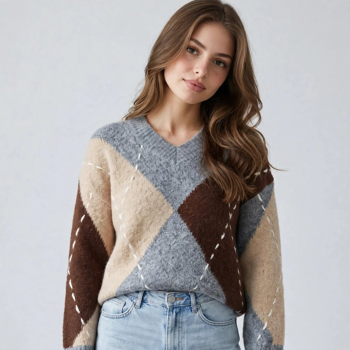 Woman in a gray argyle V-neck oversized sweater with brown diamonds, hands in jean pockets, front view, gray background.