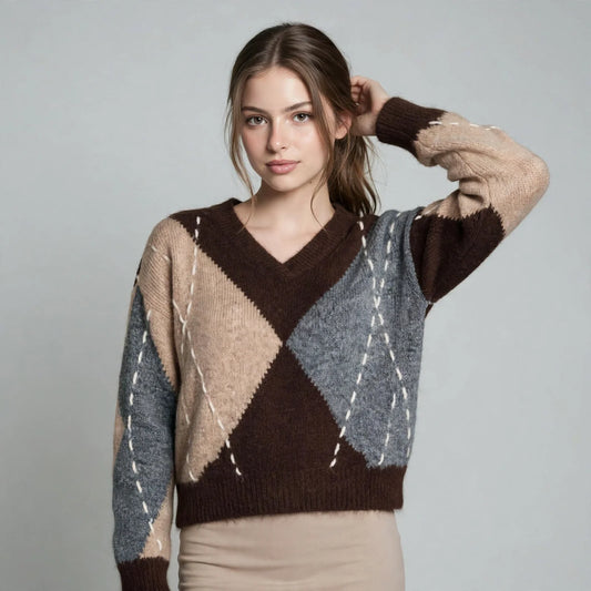 Woman in a brown argyle V-neck oversized sweater with beige and gray diamonds, hand in hair, gray studio background.