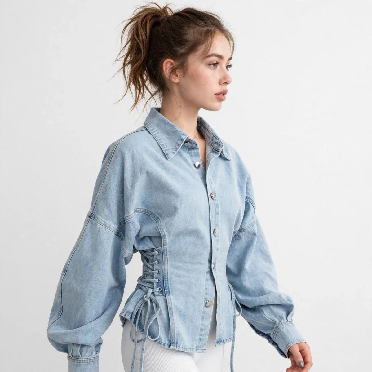 Side view of a woman wearing a light-wash denim jacket with lace-up sides and button front, white studio background.