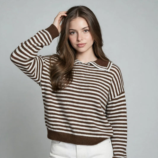 Woman in a brown and white striped knit sweater with dropped shoulders and brown trim, white pants, gray studio background.