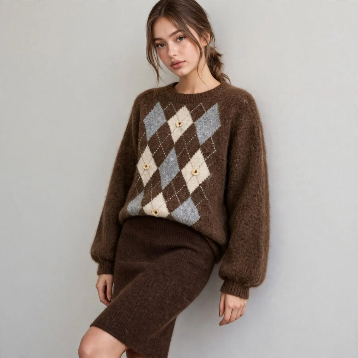 Front view of a brown argyle raglan sleeve sweater with cream and grey diamond pattern, brown skirt, white studio backdrop.