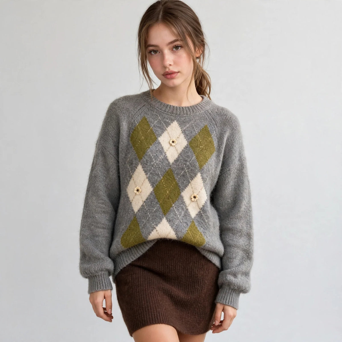 Front view of a grey argyle knit sweater with raglan sleeves and diamond pattern, brown skirt, white studio backdrop.