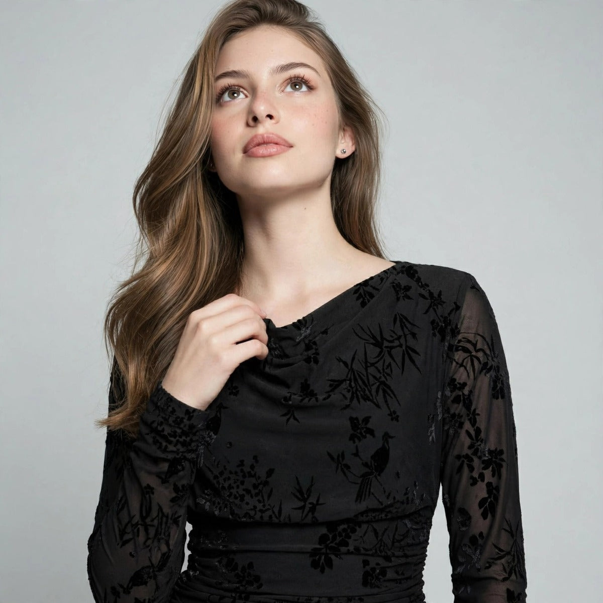 Close-up of a black long-sleeve mini dress showing floral lace texture on the bodice and draped neckline detail.