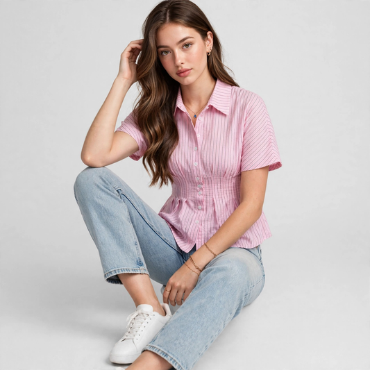 Model seated wearing a pink striped peplum button-up shirt with short sleeves, paired with jeans and white sneakers.