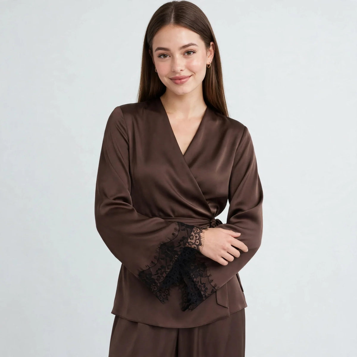 Front view of model with arms crossed wearing a chocolate brown satin wrap top with black lace cuffs and wide-leg pants