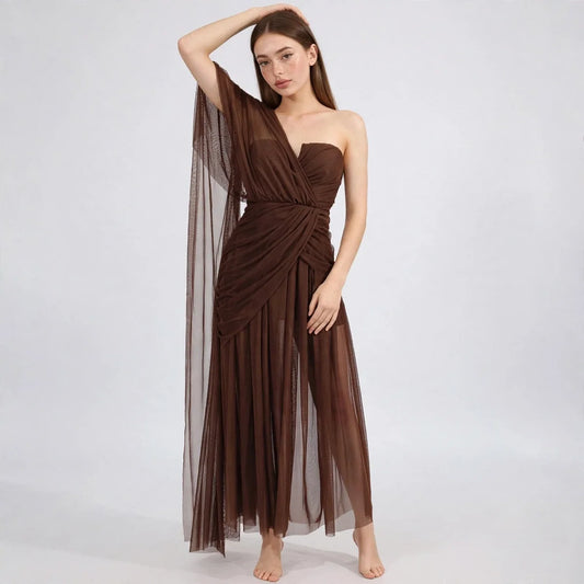 Front view of model in brown one-shoulder mesh dress with ruched bodice and sheer draped sleeve, barefoot on white background