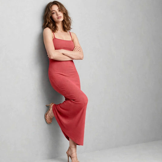 Woman leaning on a wall in a coral sleeveless maxi dress with square neckline, light studio background.
