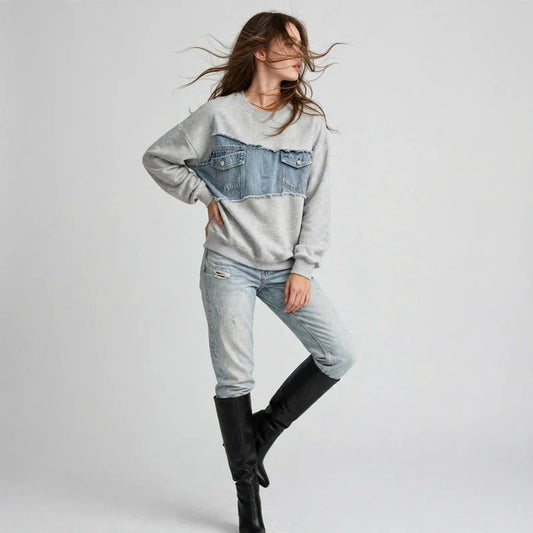 Woman posing in a gray denim-patchwork sweatshirt with light jeans and black knee-high boots, gray background.