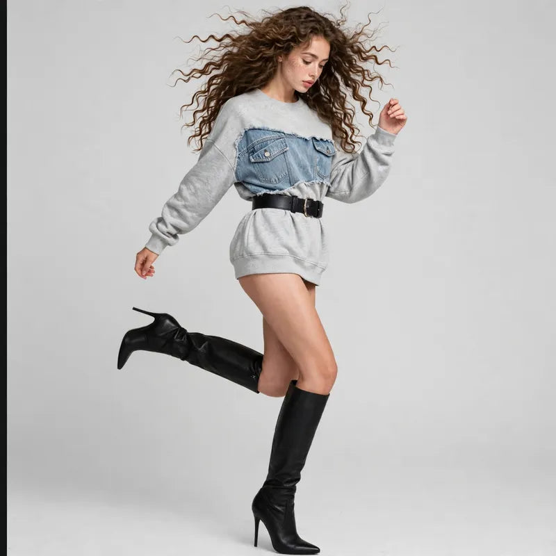 Woman jumping in a gray sweatshirt with a denim patchwork yoke, wearing black knee-high boots, light gray background.