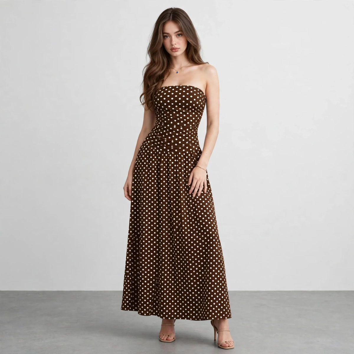 Front view of a brown polka dot strapless maxi dress with smocked bodice and flowing skirt, white studio backdrop.