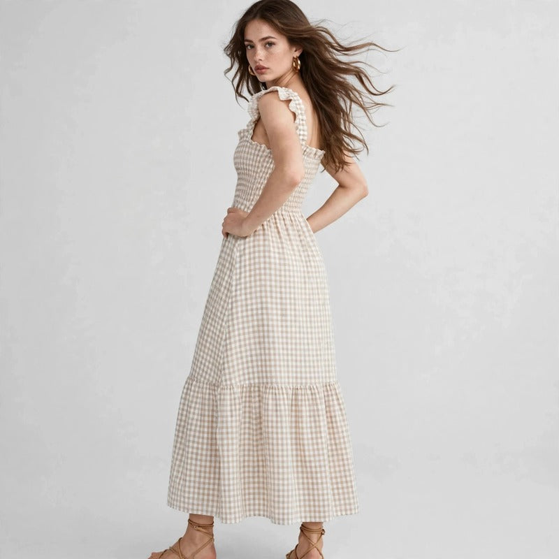 Model in beige gingham plaid maxi dress with ruffle sleeves, smocked bodice, three-quarter side view, studio backdrop.