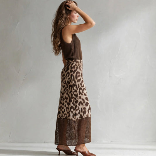 Side view of a brown sleeveless sweater dress with leopard color-block skirt panel, model with hand in hair, gray studio.