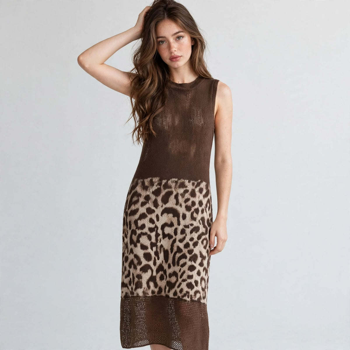 Front view of a brown sleeveless knit midi dress with leopard color-block skirt panel, model with hand in hair, studio.